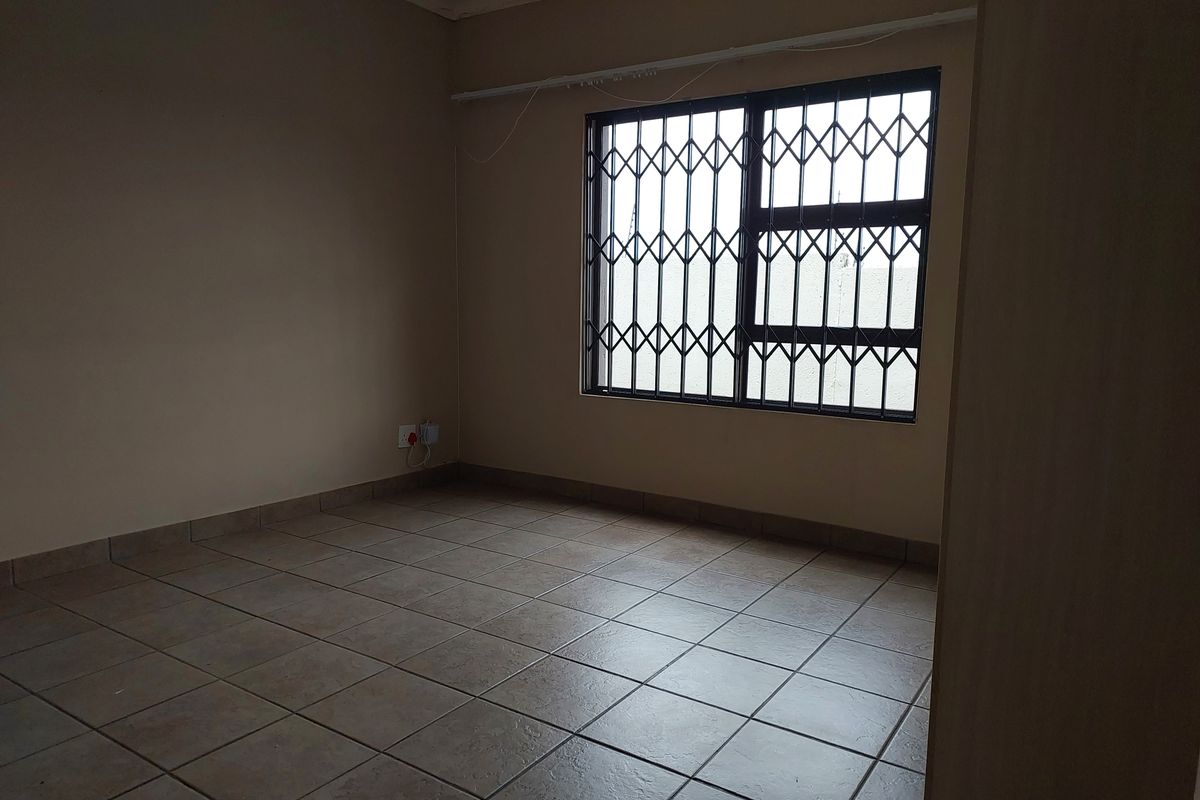 An empty bedroom featuring tiled flooring, a window with a security gate, and a built-in cupboard.