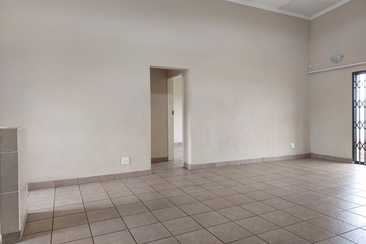 An empty, open-plan living area featuring neutral wall tones, ceramic floor tiles, and a secure metal gate leading to the exterior.