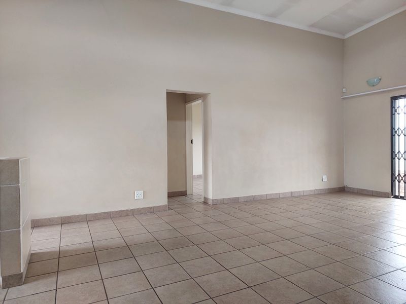 An empty, open-plan living area featuring neutral wall tones, ceramic floor tiles, and a secure metal gate leading to the exterior.
