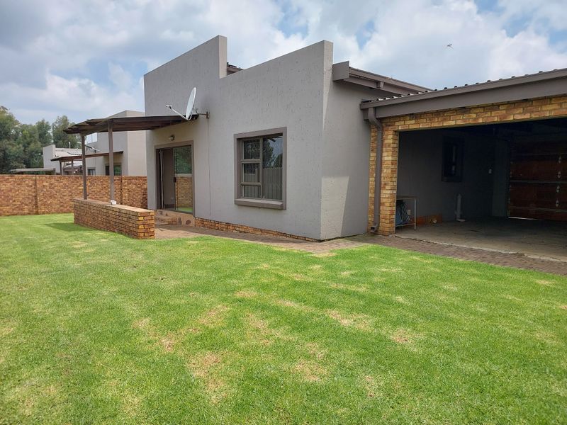Rear view of the townhouse featuring a paved patio area, covered carport, and a private garden with brick boundary walling.