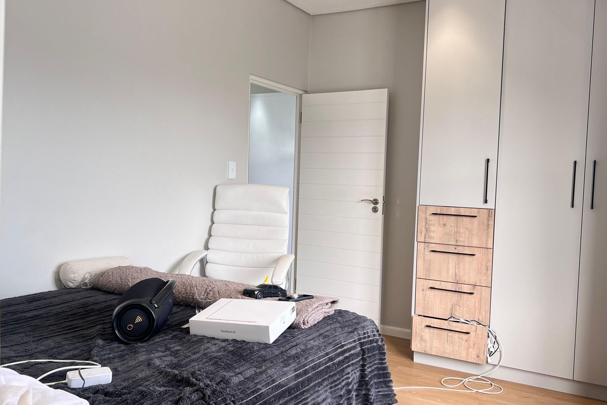 A well-maintained bedroom featuring modern built-in wardrobes with a mix of white and wood-grain finishes and light laminate flooring.