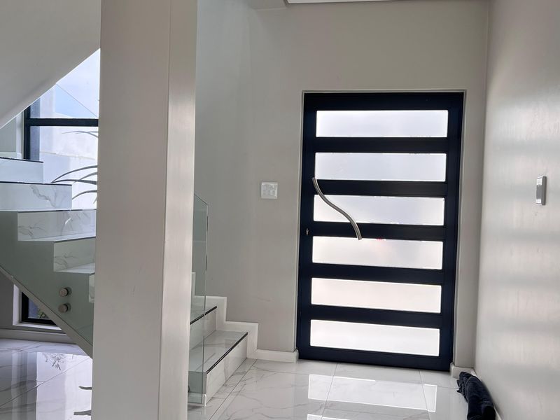Modern entrance foyer featuring a sleek staircase with glass balustrades, marble-look tiled flooring, and a contemporary front door with frosted glass panels.