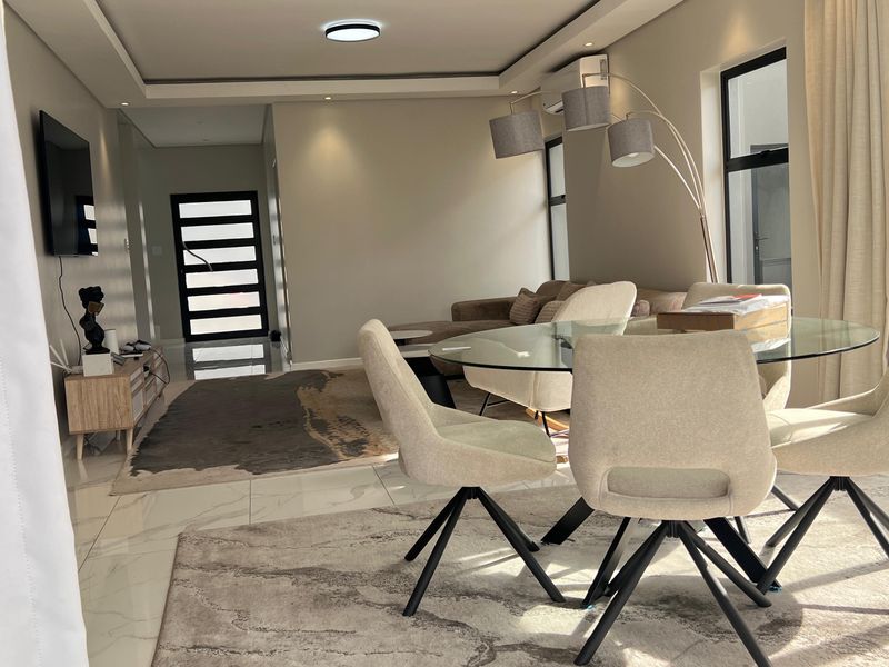 A modern open-plan living and dining area featuring sleek tiled floors, recessed ceiling lighting, and large sliding glass doors providing natural light.