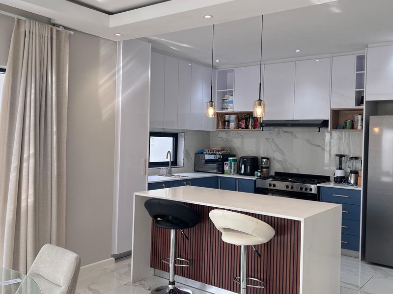 Modern kitchen featuring a central island, sleek white and blue cabinetry, marble-look splashback, and high-end integrated appliances with recessed and pendant lighting.