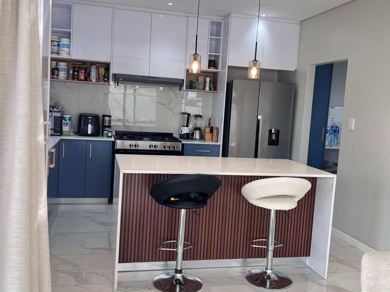 Modern kitchen featuring blue and white cabinetry, a central island with stone countertop, gas stove, and marble-look splashback, complemented by stylish pendant lighting.