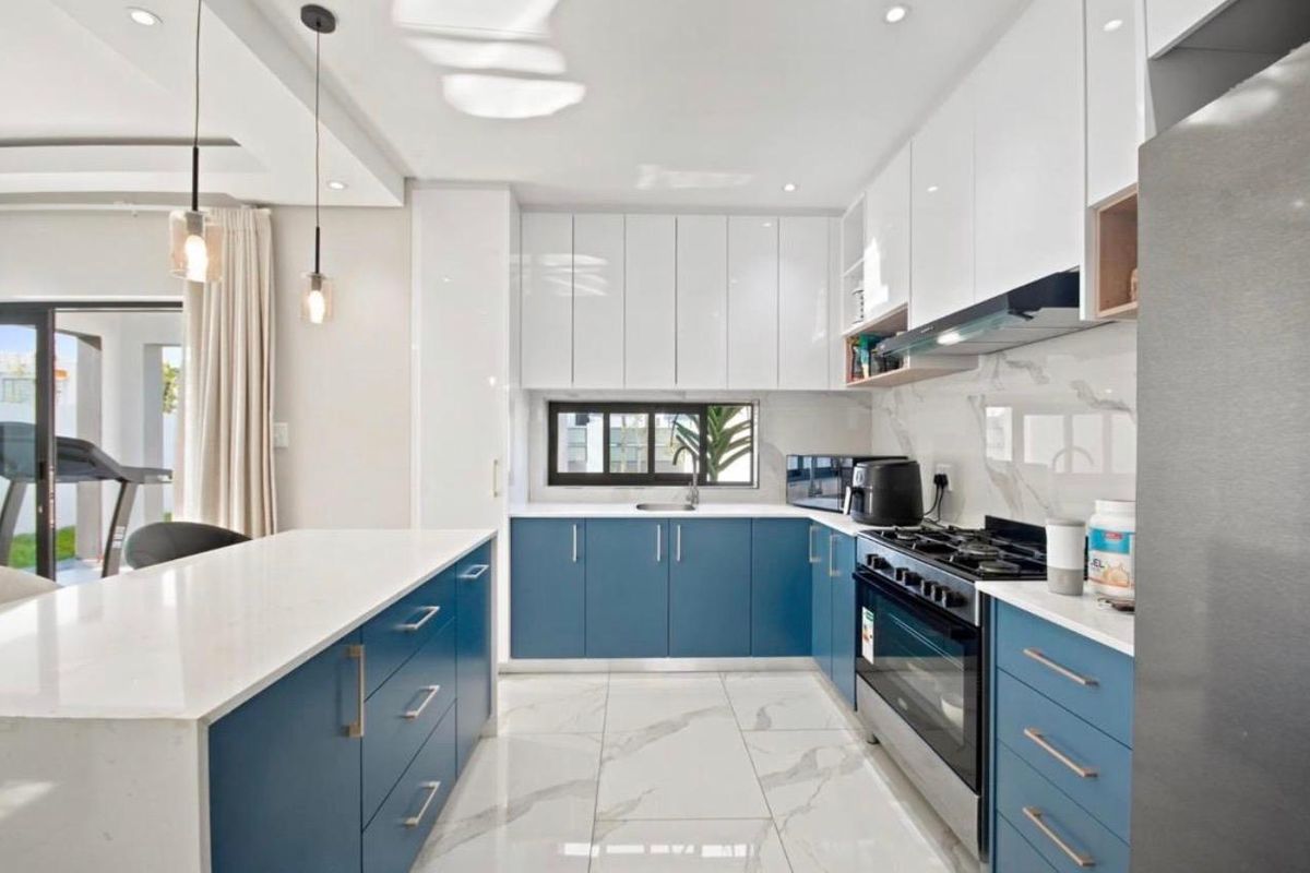 Modern kitchen featuring blue and white cabinetry, stone countertops, gas stove, extractor fan, and marble-look floor tiles with recessed lighting.