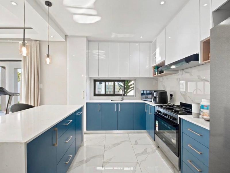 Modern kitchen featuring blue and white cabinetry, stone countertops, gas stove, extractor fan, and marble-look floor tiles with recessed lighting.