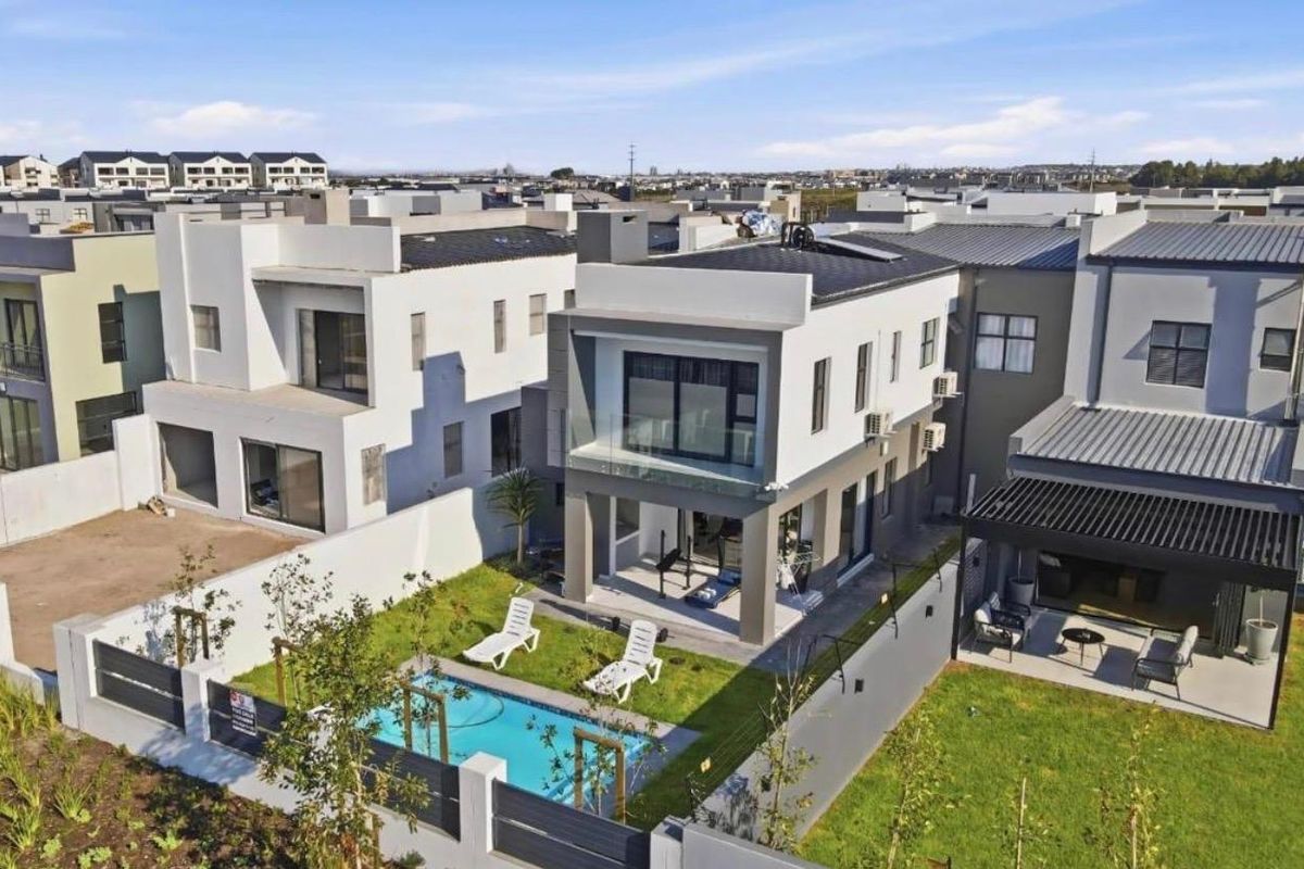 Aerial view of a modern two-story residential property featuring a private swimming pool, landscaped garden, and an upper-level balcony with glass balustrades.