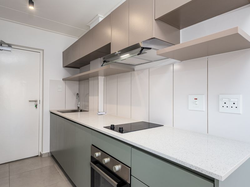 Modern kitchen featuring sleek cabinetry, stone countertops, integrated electric hob, oven, extractor fan, and a stainless steel sink.