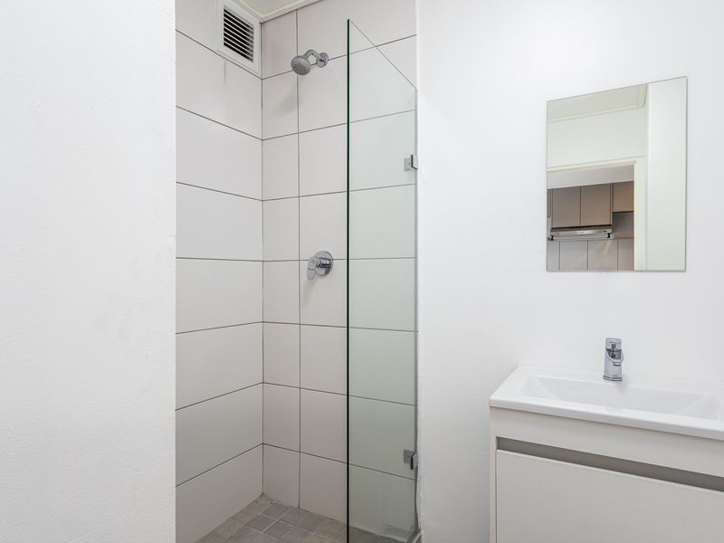 A clean, modern bathroom featuring a walk-in shower with a glass screen, a vanity basin with a mixer tap, and a wall-mounted mirror.