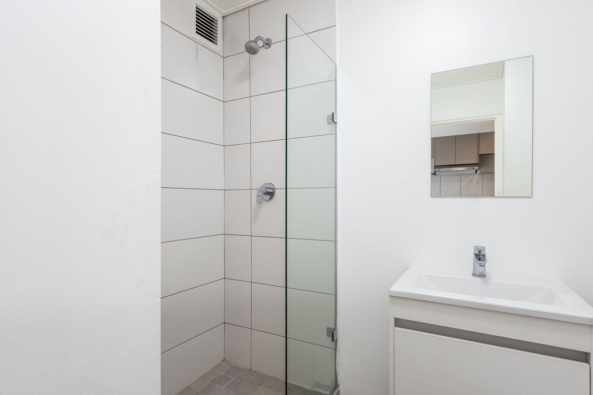 A clean, modern bathroom featuring a walk-in shower with a glass screen, a vanity basin with a mixer tap, and a wall-mounted mirror.