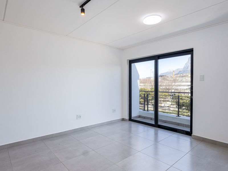 A bright, empty living area featuring neutral tiled flooring, modern track lighting, and a sliding glass door leading to a balcony with mountain views.