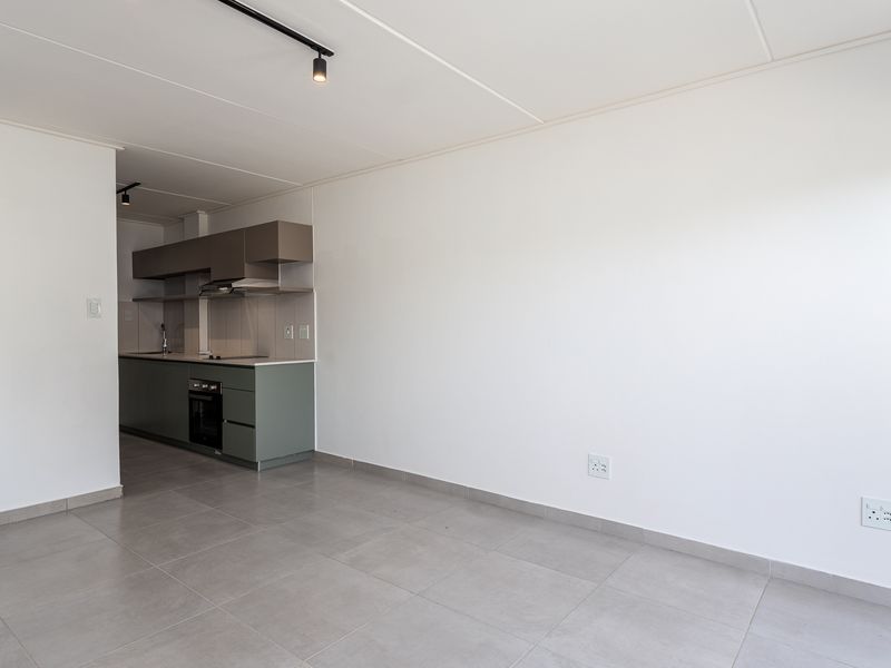 An open-plan living area featuring a modern kitchen with built-in cabinetry, integrated oven, hob, and extractor fan, finished with neutral tiled flooring.