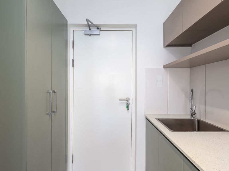 A clean and modern scullery or utility area featuring built-in cabinetry, stone countertops, a stainless steel sink, and overhead shelving.