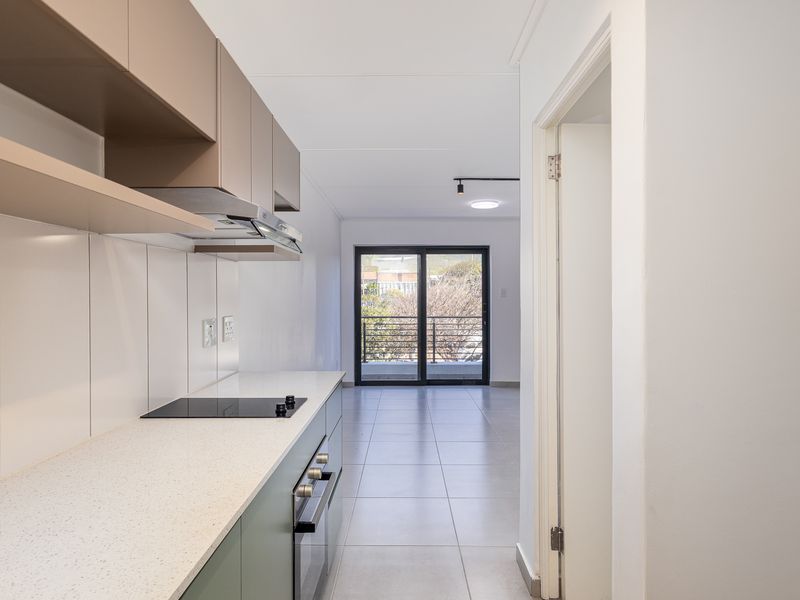 Modern kitchen featuring sleek cabinetry, stone countertops, integrated appliances, and tiled flooring, leading to an open-plan living area with balcony access.