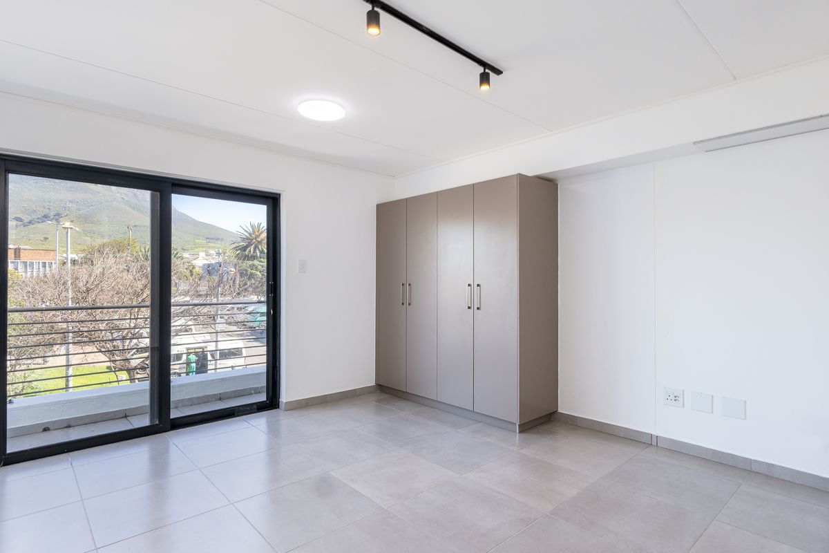 A bright, modern bedroom featuring neutral tiled flooring, built-in cupboards, and a sliding glass door leading to a balcony with mountain views.