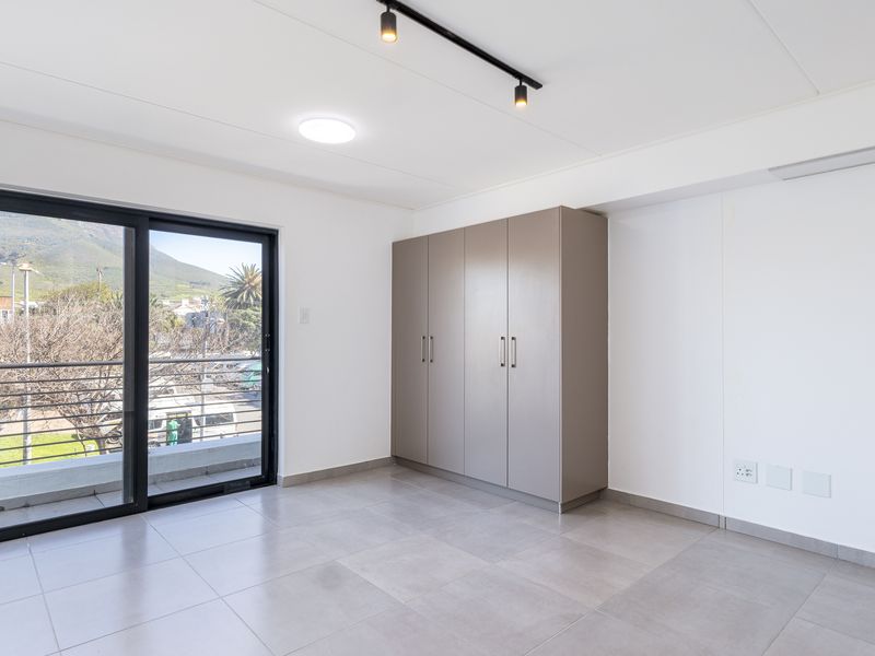 A bright, modern bedroom featuring neutral tiled flooring, built-in cupboards, and a sliding glass door leading to a balcony with mountain views.