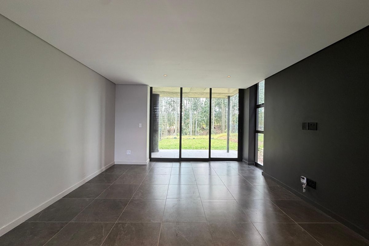 Modern, empty living room featuring large format floor tiles, a dark accent wall, and floor-to-ceiling sliding glass doors leading to the garden.