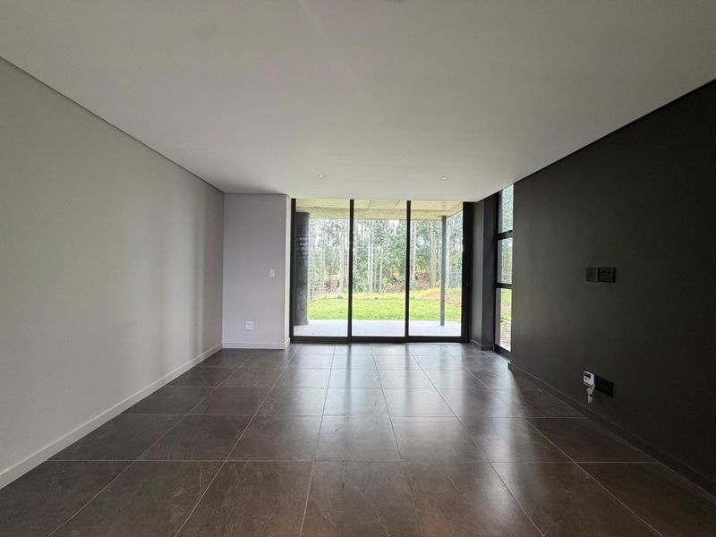 Modern, empty living room featuring large format floor tiles, a dark accent wall, and floor-to-ceiling sliding glass doors leading to the garden.