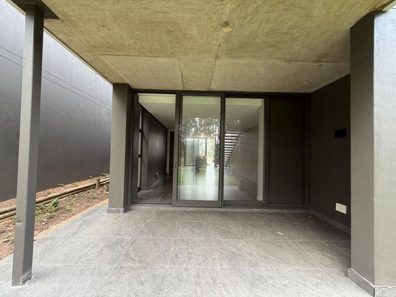 A covered patio area featuring modern tiled flooring, structural concrete ceiling, and large sliding glass doors providing access to the interior living space.