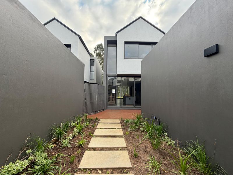 Modern townhouse entrance featuring a paved walkway, landscaped garden beds, and contemporary architectural design with large glass sliding doors.