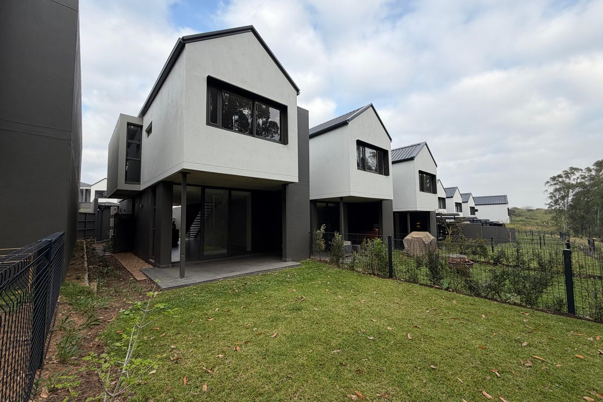 Rear view of modern townhouse units featuring covered patios, private garden spaces, and contemporary architectural design with dark and light exterior finishes.