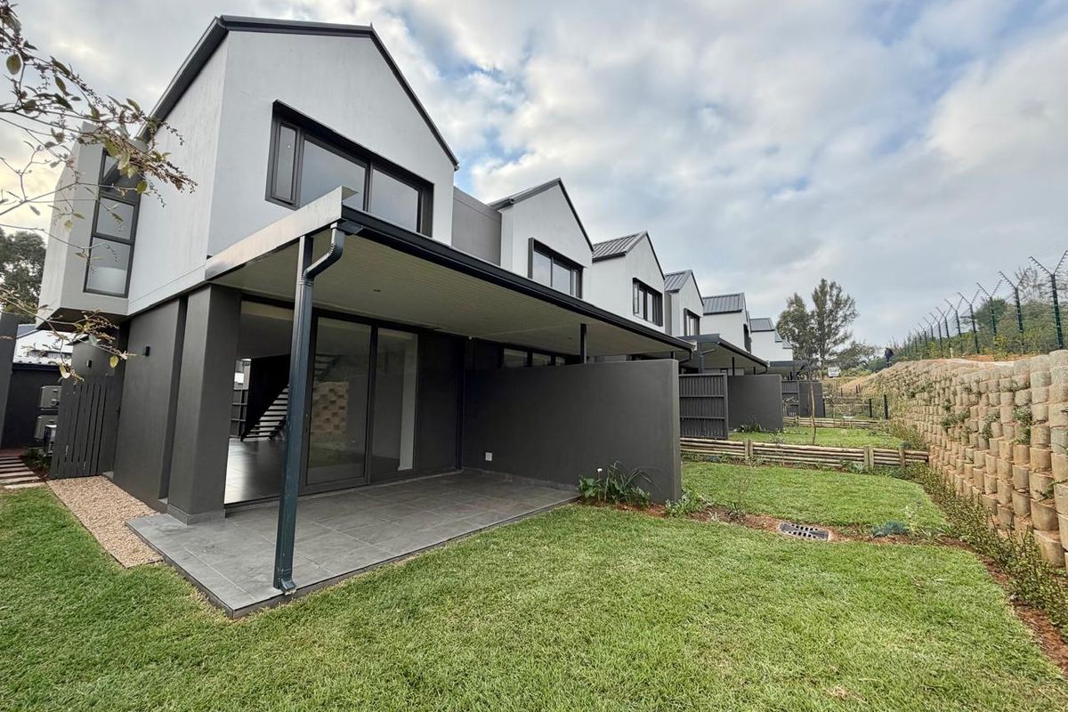 Rear view of a modern townhouse complex featuring covered patios, private garden spaces, and secure perimeter fencing.