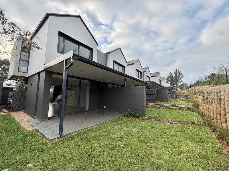 Rear view of a modern townhouse complex featuring covered patios, private garden spaces, and secure perimeter fencing.