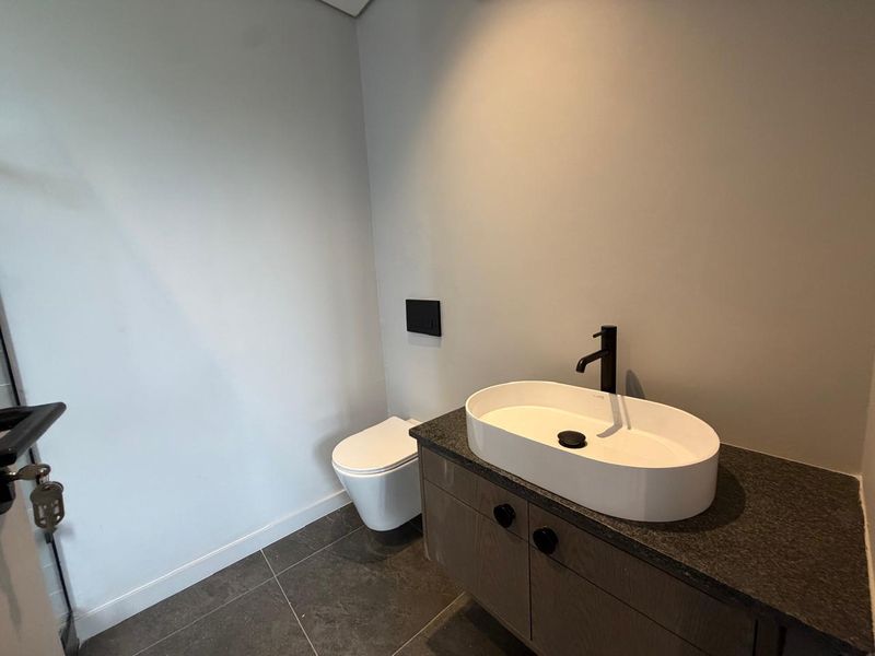 Modern bathroom featuring a wall-hung toilet, a sleek vanity cabinet with a stone countertop, and a contemporary vessel sink with black fixtures.