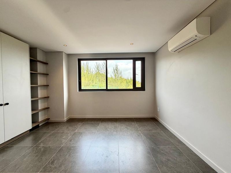A bright, modern bedroom featuring large-format floor tiles, built-in storage, open shelving, and a wall-mounted air conditioning unit.