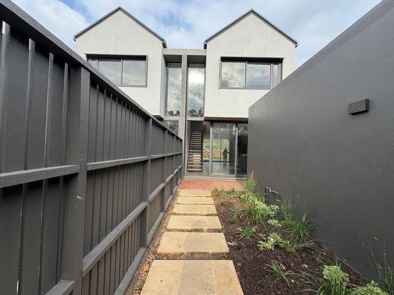 A modern townhouse rear exterior featuring a paved walkway, timber fencing, and a contemporary facade with large glass sliding doors and an external staircase.
