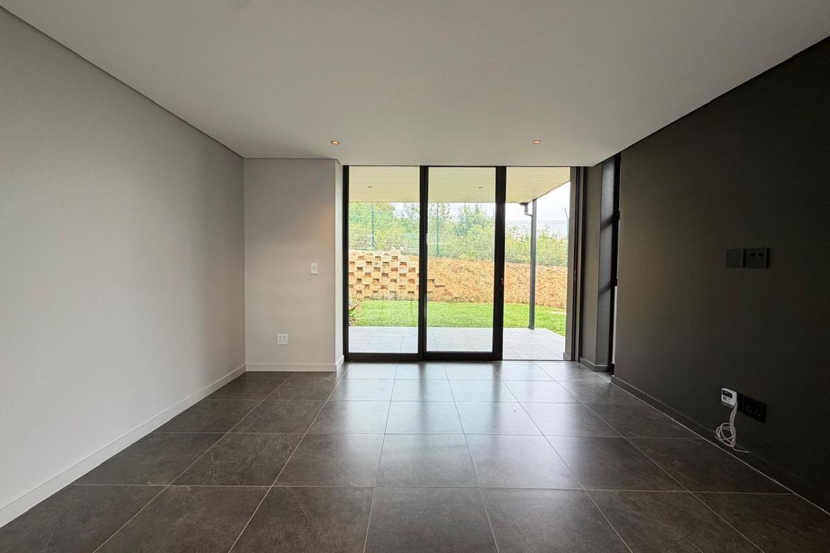 Modern, empty living area featuring large format floor tiles, a dark accent wall, and sliding glass doors providing access to the rear patio.