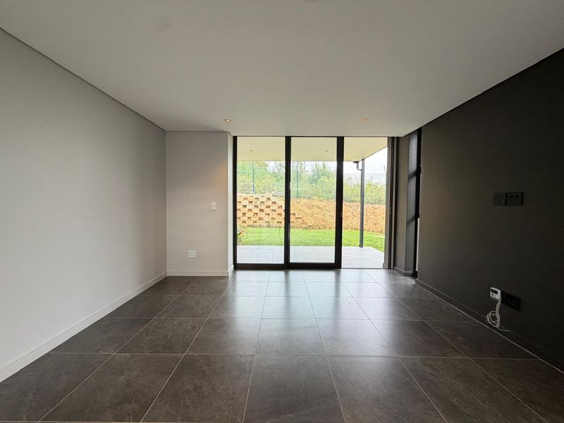 Modern, empty living area featuring large format floor tiles, a dark accent wall, and sliding glass doors providing access to the rear patio.