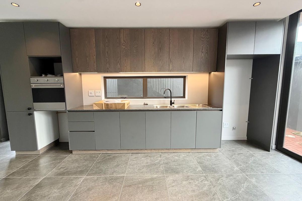 Modern kitchen featuring sleek grey cabinetry, wood-grain upper cabinets, stone countertops, integrated oven, and high-quality tiled flooring in a clean, contemporary space.