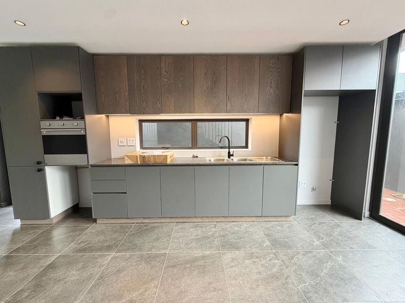 Modern kitchen featuring sleek grey cabinetry, wood-grain upper cabinets, stone countertops, integrated oven, and high-quality tiled flooring in a clean, contemporary space.