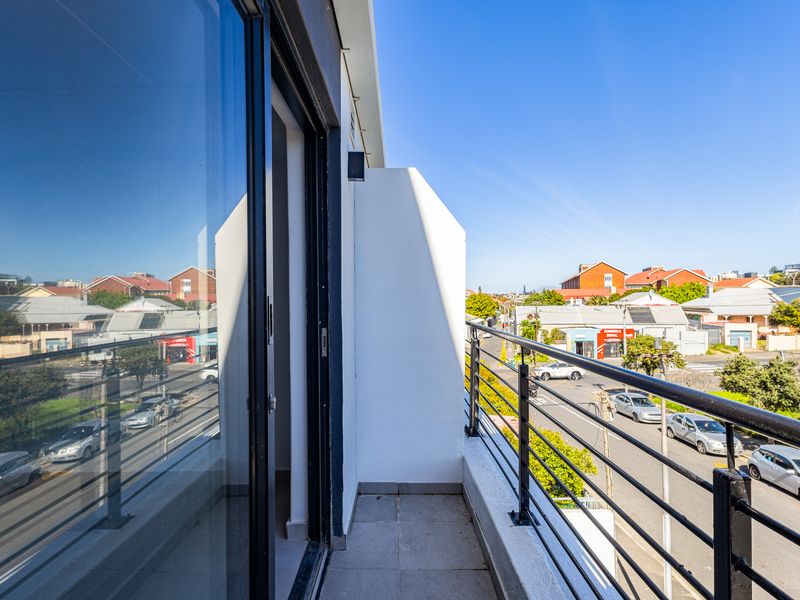 A clean, modern balcony featuring tiled flooring, a secure metal railing, and a large sliding glass door providing access to the interior.