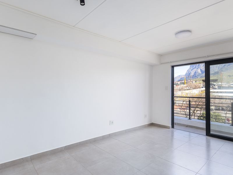 A bright, empty living area featuring neutral tiled flooring and a sliding glass door that opens onto a balcony with mountain views.