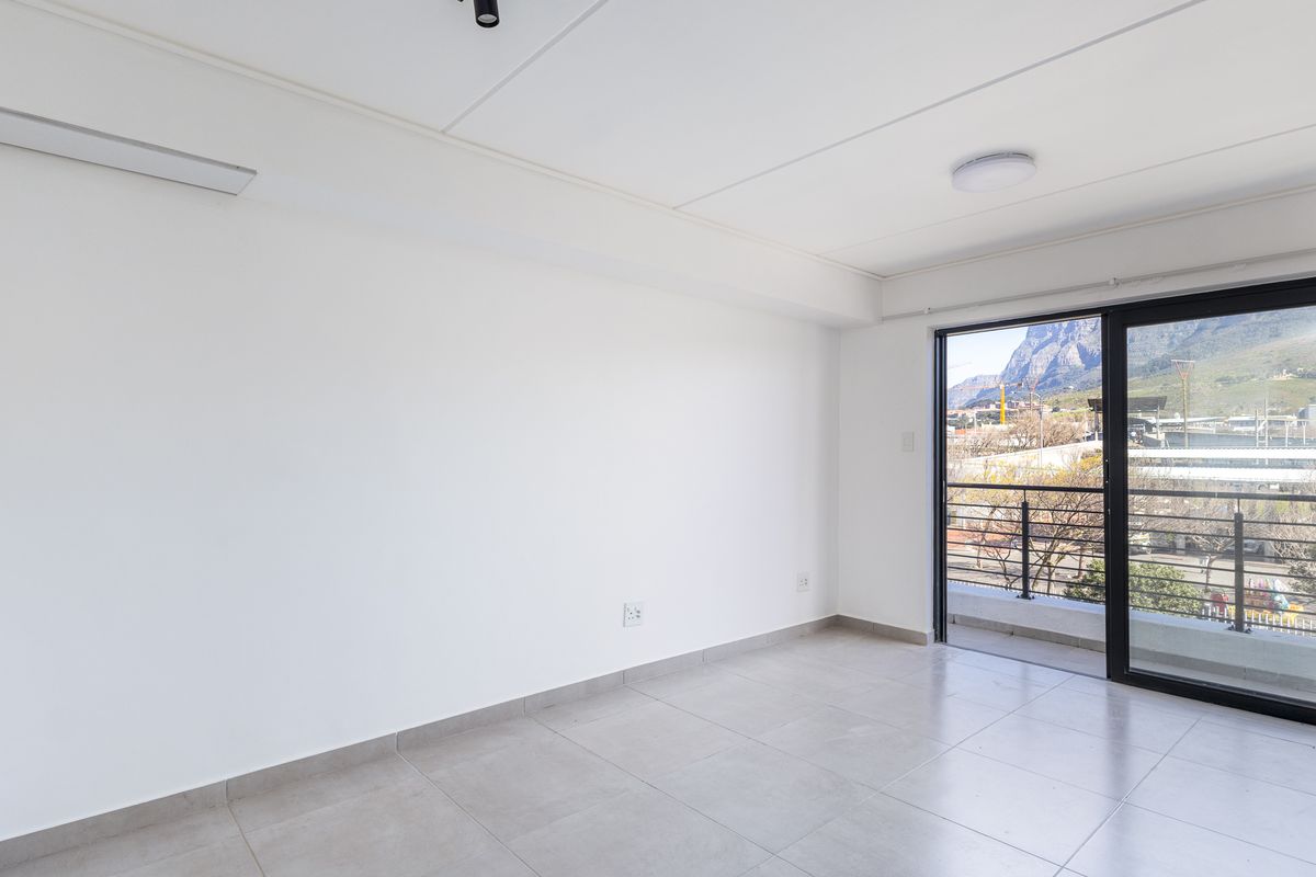 A bright, empty living area featuring neutral tiled flooring and a sliding glass door that opens onto a balcony with mountain views.