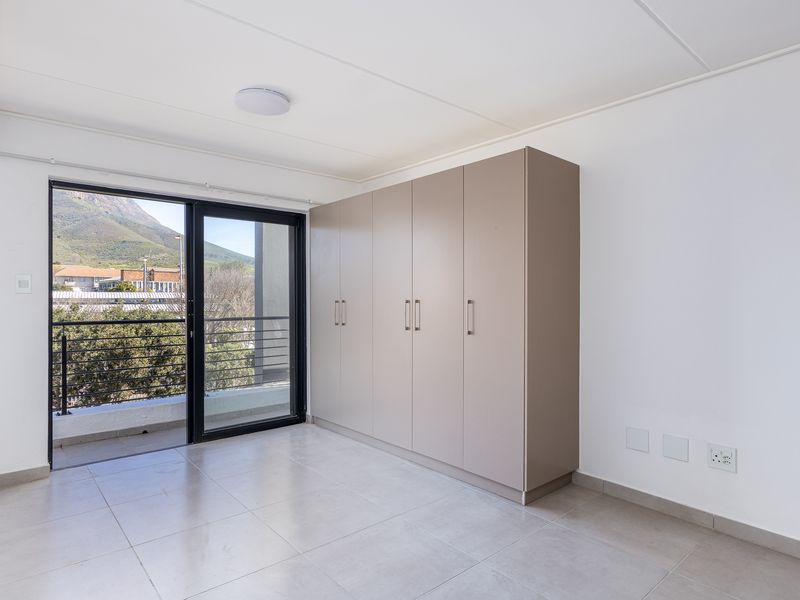 A bright, empty bedroom featuring neutral tiled flooring, ample built-in cupboards, and a sliding glass door providing access to a private balcony.