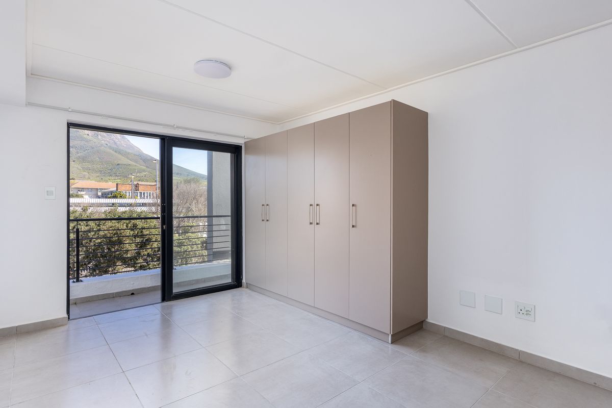 A bright, empty bedroom featuring neutral tiled flooring, ample built-in cupboards, and a sliding glass door providing access to a private balcony.