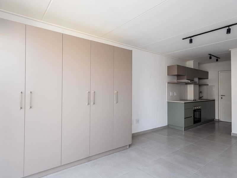 Modern open-plan apartment featuring a sleek kitchen with built-in cabinetry, oven, and extractor fan, complemented by extensive built-in storage and neutral tiled flooring.