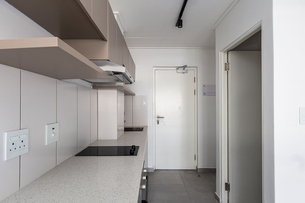 Modern kitchen featuring sleek built-in cabinetry, stone countertops, an integrated electric hob, and an extractor fan, finished with clean tiled flooring.