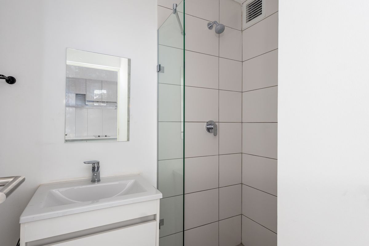 A clean, modern bathroom featuring a vanity with a basin, a glass-enclosed shower, and neutral wall tiling.