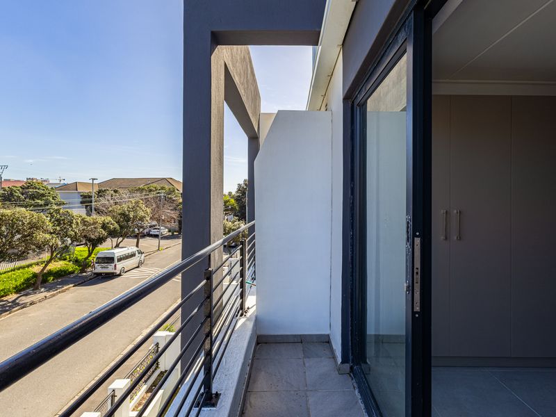 A modern balcony featuring a metal balustrade, tiled flooring, and a sliding glass door providing access to the interior living space.
