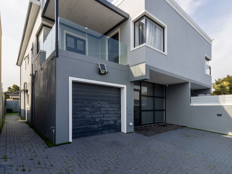 Modern townhouse exterior featuring a paved driveway, integrated garage, and a glass-balustrade balcony on the upper level.