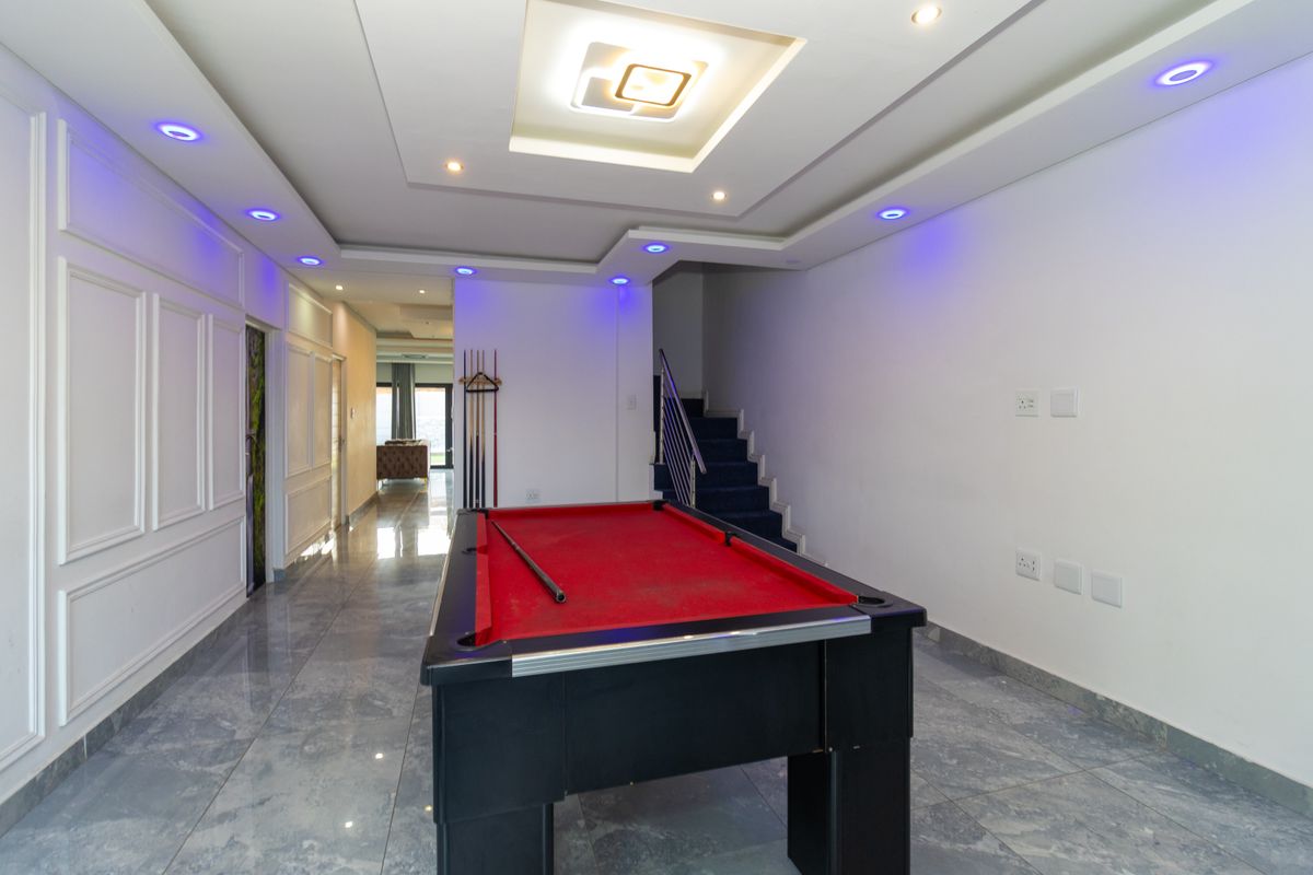Spacious living area featuring modern recessed and cove lighting, tiled flooring, and a staircase with a metal railing.