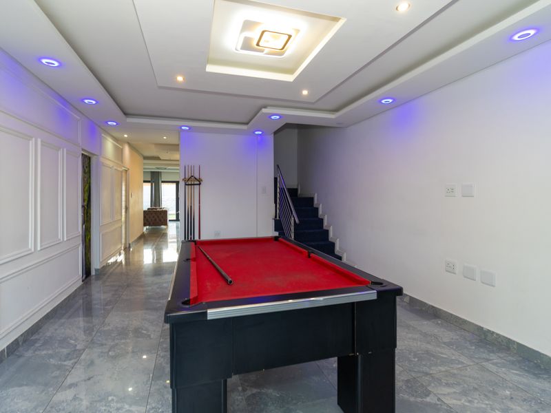 Spacious living area featuring modern recessed and cove lighting, tiled flooring, and a staircase with a metal railing.