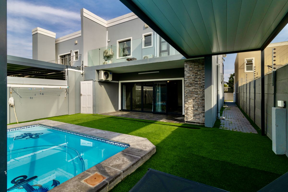 Rear exterior view of the townhouse featuring a swimming pool, artificial lawn, covered patio area, and modern stone-clad architectural detailing.