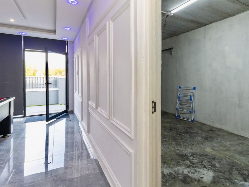 A utility space featuring wainscoting and tiled flooring, adjacent to an unfinished storage or laundry area with exposed concrete surfaces.