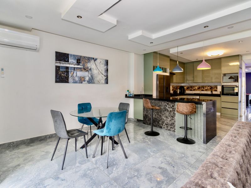 Modern open-plan living and kitchen area featuring tiled floors, a stone-topped kitchen island, built-in appliances, and recessed ceiling lighting.